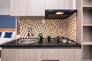 A modern kitchen with a black countertop, a gas stove, a black range hood, and a mosaic backsplash.
