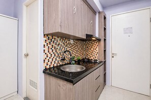 Eine Küche mit Holzschränken, einer gefliesten Spritzschutzwand, einer Edelstahlspüle und einer schwarzen Arbeitsplatte.