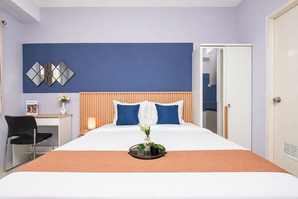 A hotel room with a bed, a desk, a chair, a mirror, and a door.