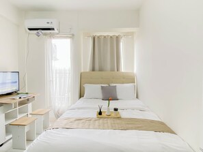 Un dormitori amb un llit, un escriptori amb ordinador, una finestra amb cortines i un aparell d'aire condicionat.