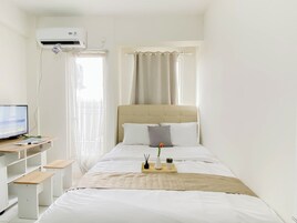 Un dormitorio con cama, un escritorio con computadora, una ventana con cortinas y un equipo de aire acondicionado.