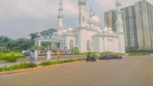 Una mezquita con múltiples minaretes y cúpulas, rodeada de vegetación y un aparcamiento con motocicletas.