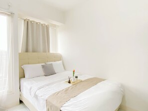 A neatly made bed with white linens, a beige throw blanket, and a small bedside table with a plant and candle.