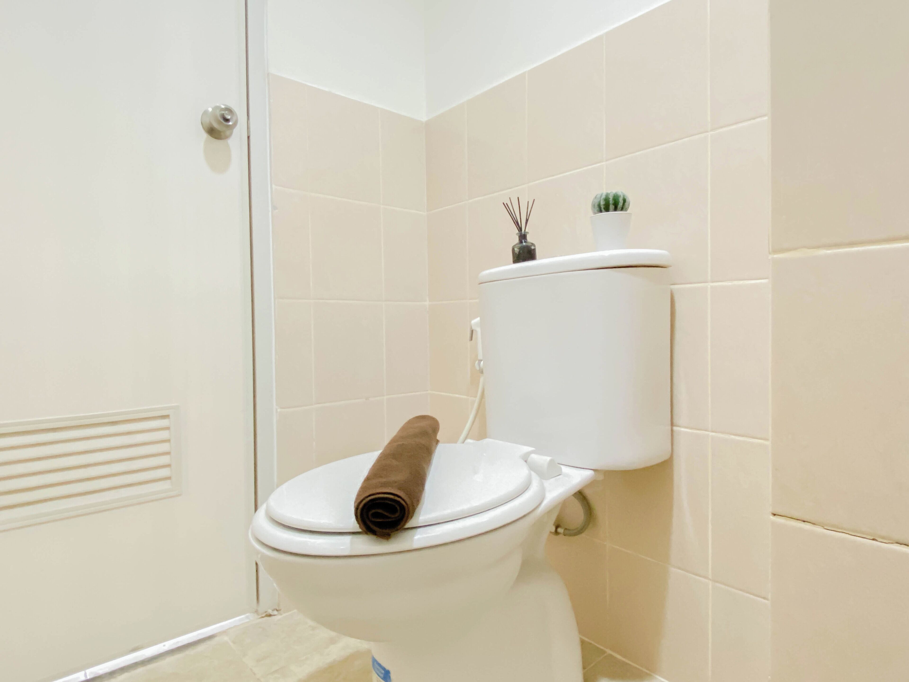 Des toilettes avec une serviette posée sur le siège, une petite plante en pot et un porte-rouleau de papier toilette fixé au mur.