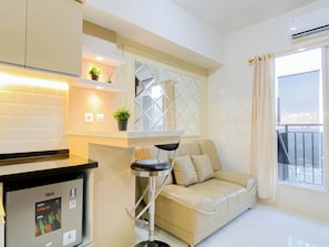 A modern living room with a sofa, a small bar area, and a window with a view. - Roomy And Warm 2Br At Apartment Podomoro Golf View (Gunung Putri)