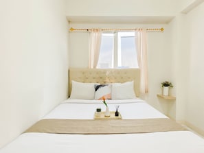 Ein Schlafzimmer mit einem Bett, einem Fenster mit Vorhängen, einem Nachttisch mit einer Vase und einer Nachttischlampe.