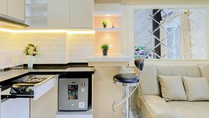 A compact kitchen with a built-in stove, a small refrigerator, and a bar stool. - Comfortable And Decent 2Br At Apartment Podomoro Golf View (Gunung Putri)