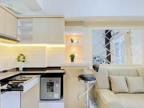 A compact kitchen with a built-in stove, a small refrigerator, and a bar stool. - Comfortable And Decent 2Br At Apartment Podomoro Golf View (Gunung Putri)