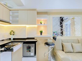 Una cocina compacta con estufa integrada, un refrigerador pequeño y un taburete de bar.