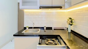 A modern kitchen with a black countertop, stainless steel sink, white cabinets, and a built-in stove. - Comfortable And Decent 2Br At Apartment Podomoro Golf View (Gunung Putri)