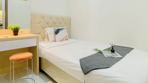 A modern hotel room with a bed, a small desk, a chair, a potted plant, and a bedside table. - Comfortable And Decent 2Br At Apartment Podomoro Golf View (Gunung Putri)