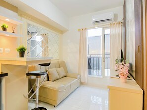 A modern living room with a sofa, a coffee table, and a TV. There is a balcony with a railing and a window. - Comfortable And Decent 2Br At Apartment Podomoro Golf View (Gunung Putri)