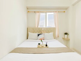 Un dormitorio con cama, ventana con cortinas, mesita de noche con un florero y lámpara de noche.