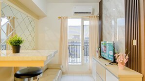 A modern kitchen with a marble countertop, a potted plant, a TV, and a balcony view. - Comfortable And Decent 2Br At Apartment Podomoro Golf View (Gunung Putri)