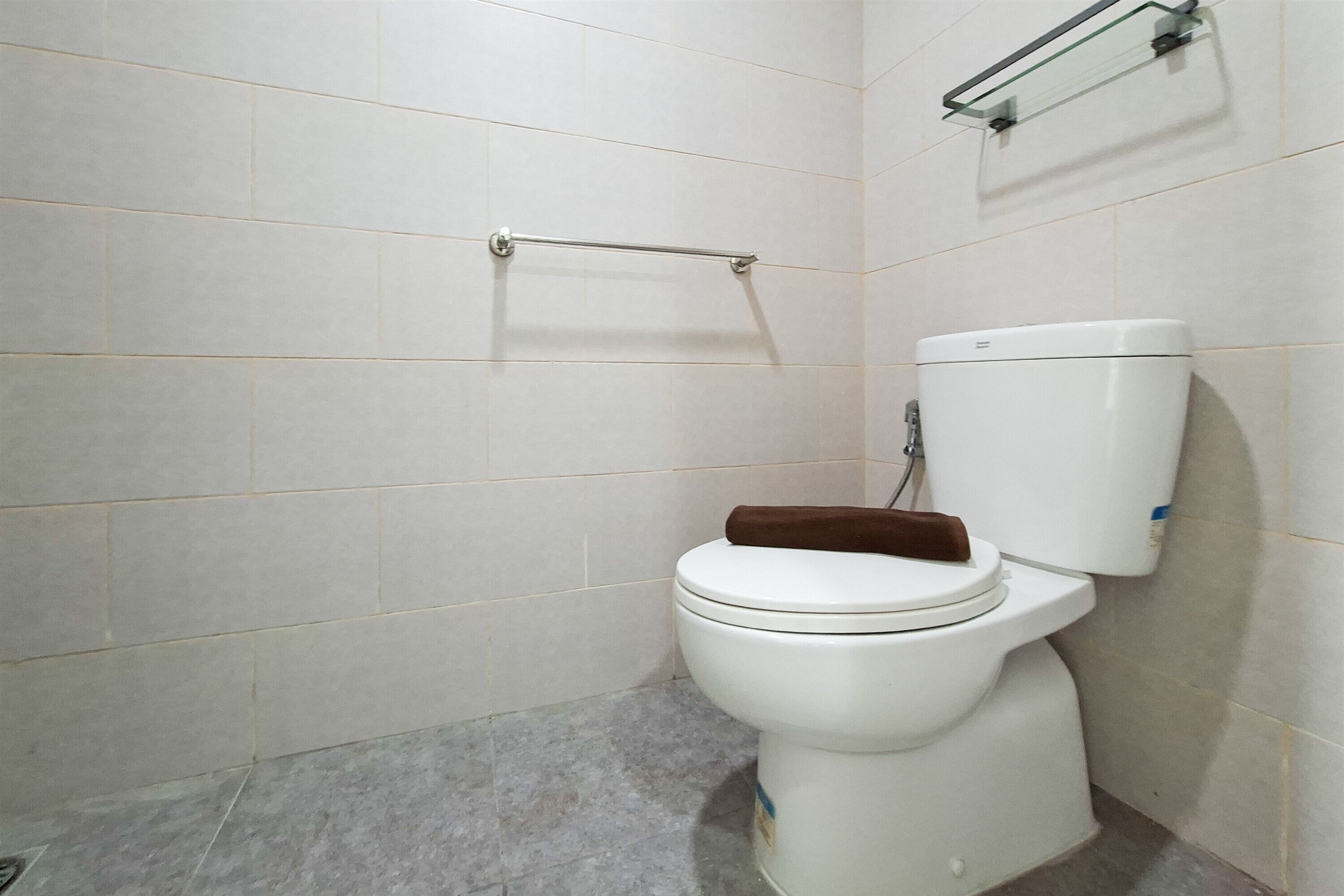 Une salle de bain avec des toilettes blanches, un abattant marron et une étagère en verre au-dessus des toilettes.