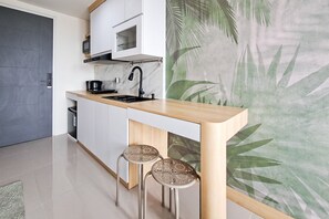 A modern kitchen with a wooden countertop, two stools, a microwave, and a stove. - Bright And Cozy Studio Room At Apartment Samesta Mahata Serpong (South Tangerang)