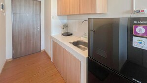 A kitchen with a black refrigerator, wooden cabinets, a white countertop, and a stainless steel sink. - Compact Studio Apartment For 2 Pax At Sentraland Medan (Medan)