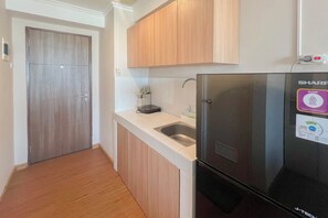 A kitchen with a black refrigerator, wooden cabinets, a white countertop, and a stainless steel sink. - Compact Studio Apartment For 2 Pax At Sentraland Medan (Medan)