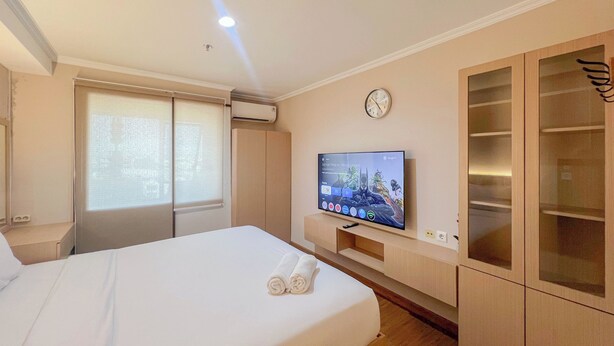 A hotel room with a bed, a TV, a clock, and a wardrobe. - Compact Studio Apartment For 2 Pax At Sentraland Medan (Medan)