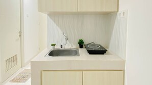 Una cocina pequeña con un lavamanos, un grifo, una pequeña planta en maceta, una caja negra y armarios de tonos claros.