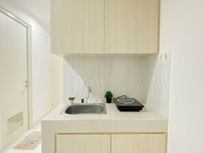 A small kitchen with a sink, a faucet, a small potted plant, a black box, and light-colored cabinets. - Serene 1Br For 2 Pax At Sentul Tower Apartment (Citaringgul)