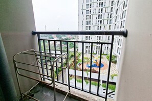 Un balcone con ringhiera in metallo, una sedia e vista su una zona residenziale con edifici e un'area giochi.