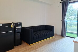 Et værelse med en sort sofa, et sort køleskab og et vindue med gardiner.