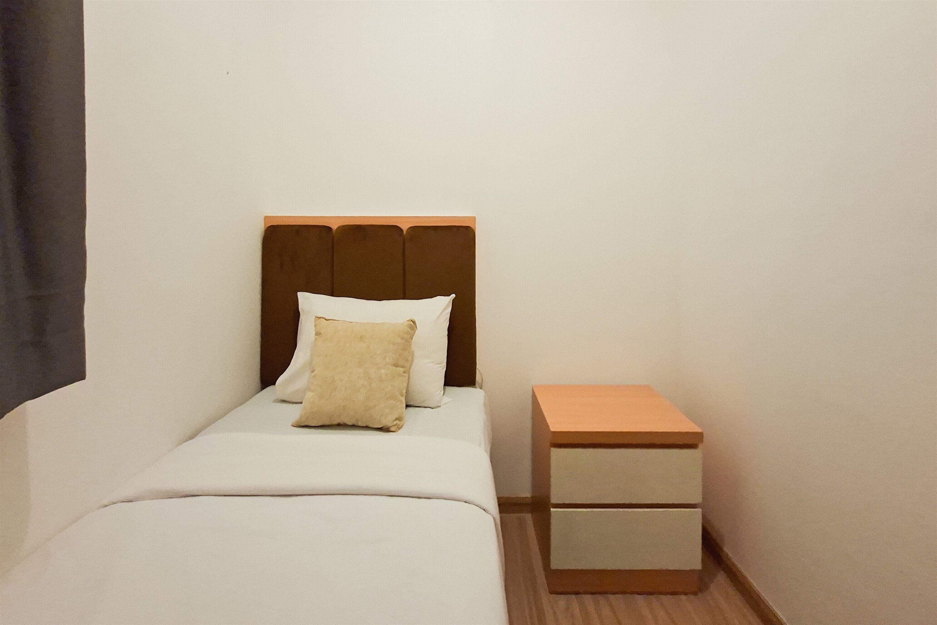 Una cama individual con cabecera de madera, una mesita de noche con cajones y una pared lisa.