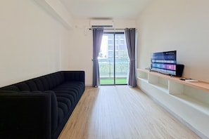 Una sala de estar moderna con un sofá negro, un televisor en un estante de madera y una puerta corrediza de vidrio al exterior.