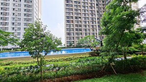Zona residencial con piscina, abundante vegetación y edificios de apartamentos altos al fondo.