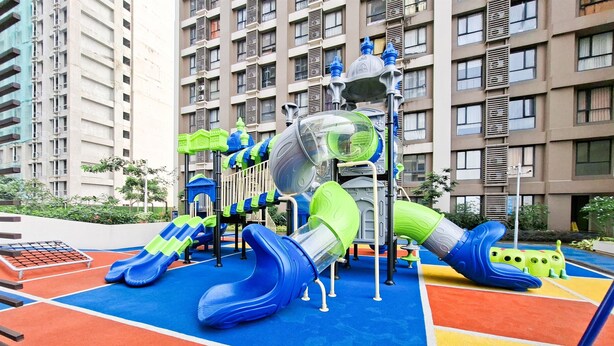 Un parque infantil con toboganes y estructuras para escalar, rodeado de una zona de juegos de colores y edificios residenciales altos al fondo.