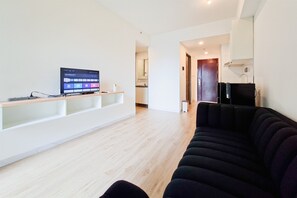 Una sala de estar moderna con un televisor de pantalla plana, un sofá negro y piso de madera.