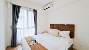 Una habitación de hotel con cama, mesita de noche, equipo de aire acondicionado y ventana con cortinas.