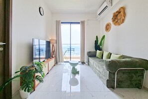 A modern living room with a flat-screen TV, a sofa, a coffee table, and a potted plant. - 3 Pax Tranquil 2Br At Sky House Bsd Apartment (Pagedangan)
