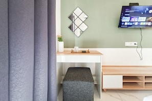 Habitació moderna amb escriptori, televisió penjada a la paret, una banca i presa elèctrica.