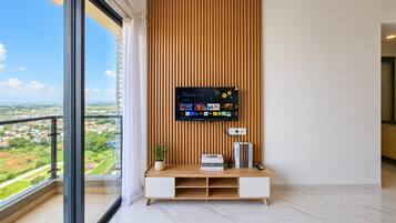 Una sala moderna con un televisor grande montado en una pared de paneles de madera, un mueble blanco de entretenimiento debajo y un balcón con vista a la ciudad.