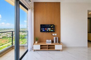 Una sala moderna con un televisor grande montado en una pared de paneles de madera, un mueble blanco de entretenimiento debajo y un balcón con vista a la ciudad.