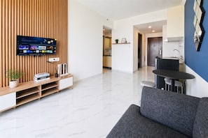 Ein modernes Wohnzimmer mit einem Flachbildfernseher, einem grauen Sofa, einer Holz-Unterhaltungseinheit und einer Küche im Hintergrund.