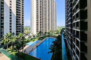 A high-rise residential building with a swimming pool surrounded by palm trees and greenery. - Studio Apartment With Functional Design At Sky House Bsd (Pagedangan)