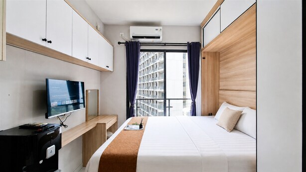 Una camera d'albergo con un letto, una TV, un minibar e una finestra con tende.