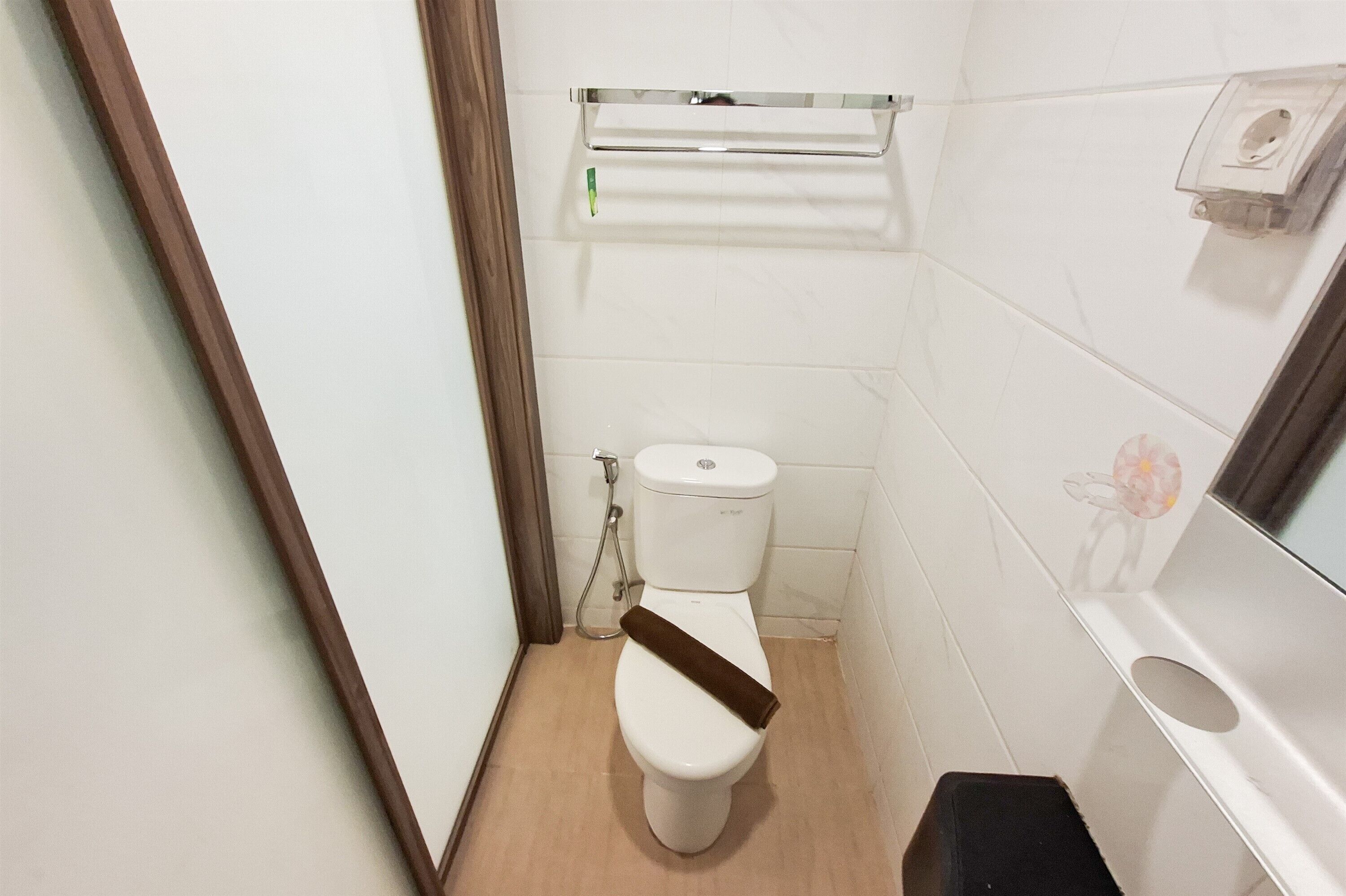 A small bathroom with a toilet, a shower, a towel rack, and a trash bin.