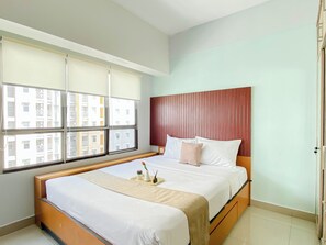 Habitació d'hotel amb un llit gran, un panell de capçalera de fusta i vista als edificis a través de la finestra.