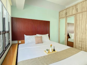 Quarto de hotel com uma cama, cabeceira de madeira, um guarda-roupa e uma janela com persianas.