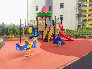 Um parquinho com diversas estruturas de recreação, incluindo balanços e escorregadores, cercado por uma superfície de segurança vermelha.