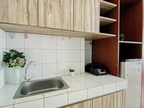 Cuina amb rajoles blanques, un vàter d'acer inoxidable, armaris de fusta i un frigorífic.