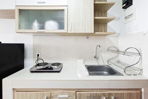 A kitchen with a stove, sink, and wooden cabinets. - Simply Minimalist Studio Apartment Springwood Residence Tangerang (Tangerang)