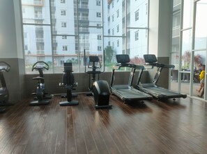 A gym with exercise equipment, large windows, and a view of residential buildings. - Convenient Studio Apartment Suncity Residence (Sidoarjo)