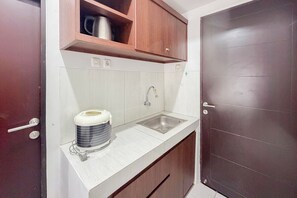 A compact kitchen with a sink, a coffee maker, and wooden cabinets. - Convenient Studio Apartment Suncity Residence (Sidoarjo)