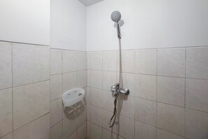 Une douche équipée d’un pommeau de douche à main et d’un robinet mural, d’un porte-savon en plastique blanc et de murs carrelés.
