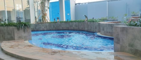 Una piscina de borde curvo, rodeada por un muro de piedra bajo y escalones que bajan al agua.